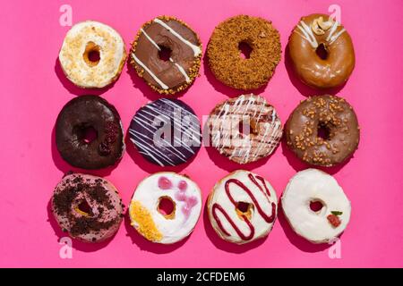 Draufsicht auf Sortiment von leckeren süßen glasierten Donuts dekoriert Mit Glasur und Schokolade und verschiedenen Arten von Streuseln auf Leuchtender rosa Hintergrund Stockfoto