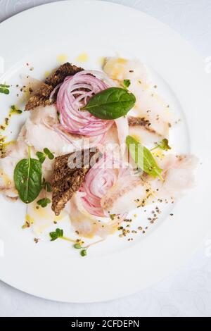 Blick von oben auf exquisite appetitliche Gericht mit Fisch und Zwiebeln Ringe garniert mit frischen Basilikumblättern und Toast serviert auf Weiße Platte Stockfoto