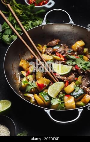 Von oben der asiatischen würzigen Wok rühren gebratene Gericht mit Fleisch und Zucchini garniert mit frischer Limette und Koriander Stockfoto