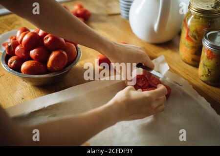 Ernte Hausfrau Putting schneiden frische Tomaten auf Backblech während Zubereitung von traditionellen hausgemachten Eingemachtes am Holztisch in der Küche Stockfoto