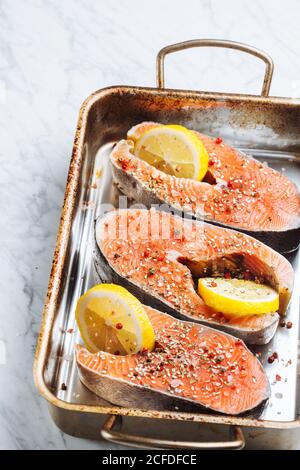 Blick von oben auf frische Lachssteaks mit aromatischen Gewürzen und Zitronenscheiben auf Blech legen Stockfoto