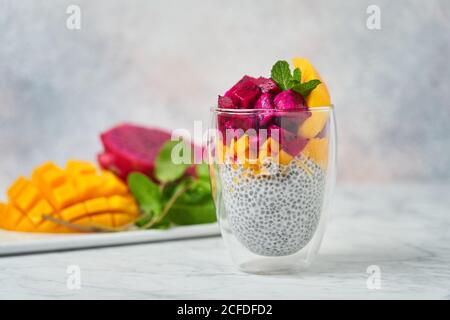 Chia Pudding mit Scheiben von Mango roten Pitaya und dekoriert Frische Minze im Glas mit frischen Zutaten auf verschwommenem Hintergrund Stockfoto