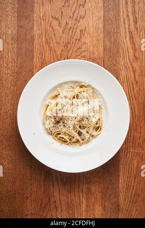 Blick von oben auf den weißen Teller mit gekochten Spaghetti und geriebenen Käse auf Holztisch Stockfoto