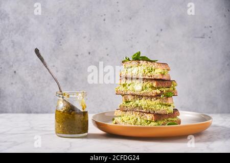 Stapel Roggenbrot Sandwiches mit Avocado-Püree serviert mit Frische Minze auf dem Tisch mit Glas Pesto-Sauce Stockfoto