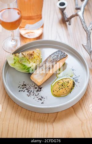 Gedämpfter Lachs mit gegrilltem Kohl auf weißem Keramikplatte serviert Auf Holztisch mit Glas und Flasche Wein Stockfoto