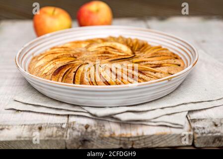 Apfelkuchen in runder Form gebacken und mit Apfelscheiben verziert, mit zwei Äpfeln verziert Stockfoto