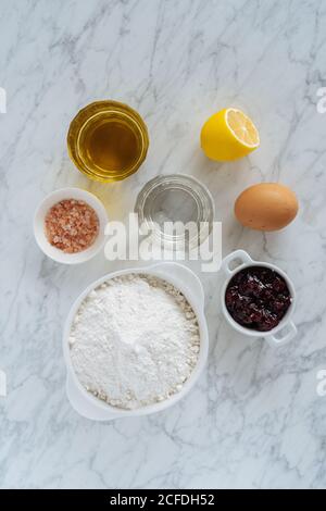Draufsicht auf Satz von Zutaten für Backen Rezept einschließlich Weißmehl und Ei und Gläser mit flüssigen Produkten mit Zitrone und Salz auf Marmorboden Stockfoto