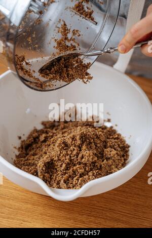 Ernte Hausfrau mit Löffel setzen gemahlene braune Linse aus dem Essen Prozessor in große weiße Schüssel auf Holztisch platziert Stockfoto