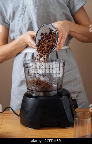 Crop weiblich in grau Schürze setzen eingeweichte Linsen aus Schüssel An die Küchenmaschine beim Zubereiten des Abendessens am Holztisch hinein Küche Stockfoto