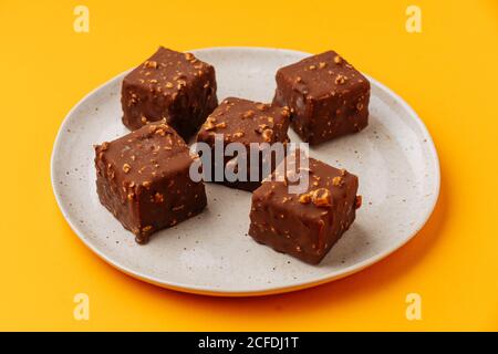 Von oben lecker kubische Kekse mit Schokolade Zuckerguss und dekoriert Muttern und auf Platte auf gelbem Hintergrund platziert Stockfoto