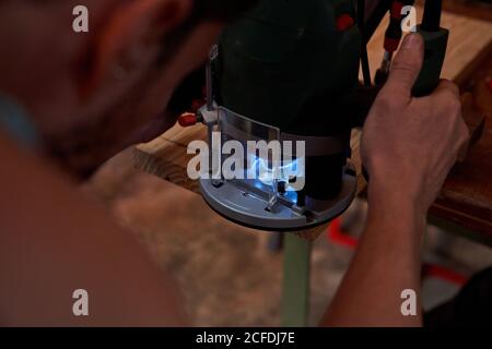 Crop man mit Fräsmaschine für die Verarbeitung von Holzbrett während Arbeiten am Arbeitsplatz Stockfoto