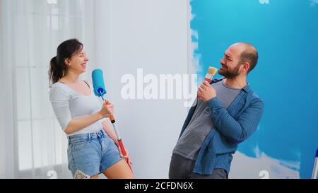 Paar voller Glück, während sie ihre Wohnung eine Renovierung. Singen auf dem Bürstenrolle. Wohndekoration und Renovierung in gemütlichen Wohnung Wohnung, Reparatur und Verjüngungskur Stockfoto