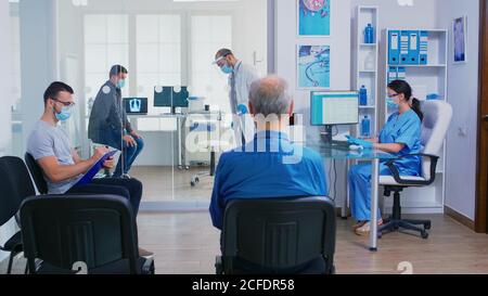 Arzt, der Krankenschwester Patienten Radiographie während der Beendigung der kranken Mann Untersuchung in seinem Büro. Assistent mit Gesichtsmaske gegen covid-19 schieben behinderte Frau im Rollstuhl durch Wartebereich. Stockfoto