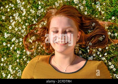 Junges Mädchen mit rötlich gespreizte Haare liegt auf Wiese mit weißen kleinen Blumen, Porträt Stockfoto