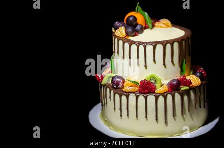 Schöne zweistufige Kuchen mit Schokolade gegossen und mit frischen Früchten auf schwarzem Hintergrund dekoriert. Stockfoto