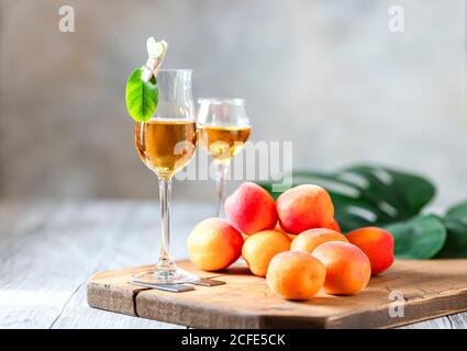 Aprikosenlikör in Schrotglas und frische Aprikosen auf einem hellen Holztisch. Stockfoto