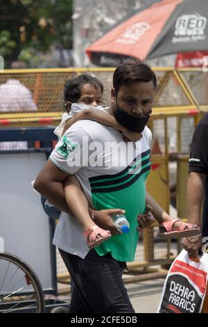 Dehradun, Uttarakhand/Indien - August 15 2020: Männer mit Kind auf dem Rücken, Maske tragend, Kamera zugewandt. Stockfoto