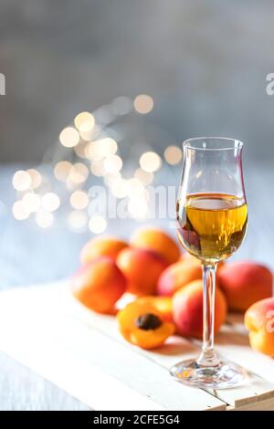 Aprikosenlikör im Schnapsglas und frische Aprikosen auf dem hellen Holztisch im Urlaub buntes Bokeh. Stockfoto