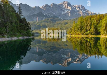 Blick über die Sasseninsel (Sassenbüchel, Roseninsel) auf den Eibsee zur Zugspitze bei Sonnenaufgang, blauer Himmel, türkisfarbenes (grünes) Wasser, Spiegelung, Bäume, Stockfoto