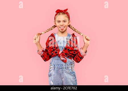 Freistil. Kleines Mädchen in Bandana auf dem Kopf stehend isoliert auf rosa halten Zöpfe posieren Kamera verspielt Stockfoto