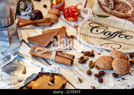Cinammon-Sticks mit Juteseil, Kaffeekanne, Süßigkeiten und Keksen auf weißem Holzhintergrund gebunden. Kaffeepause oder Frühstück im Hintergrund. Stockfoto