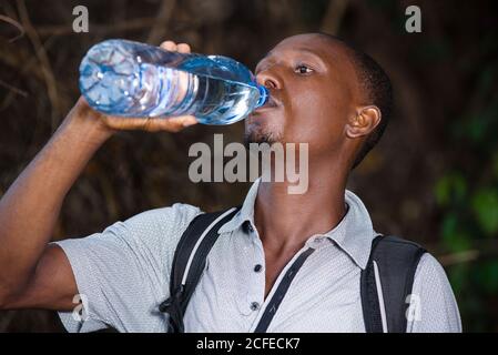 Junger Mann in grauem T-Shirt stehend Trinkwasser in einer Plastikflasche. Stockfoto