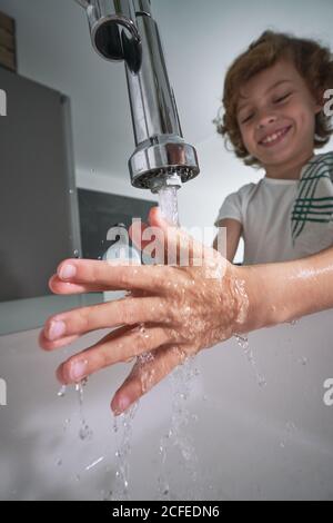 Von unten Junge mit Handtuch auf der Schulter waschen Hände unter Fließendes Wasser sorgfältig im modernen Badezimmer zu Hause Stockfoto