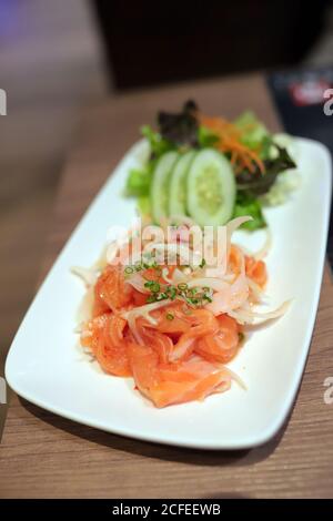 Lachsfilet im Thai-Stil würziger Salat auf weißem Teller auf Holztisch im japanischen Restaurant. Selektiver Fokus. Stockfoto