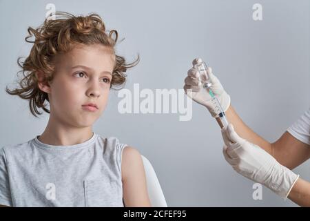 Unkenntlich Crop Arzt in Latex-Handschuhe Füllung in Spritze mit Impfstoffmedikament aus der Flasche, die für die Injektion in der Schulter vorbereitet Junge mit lockigen Haaren Stockfoto