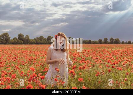 Junges Mädchen mit rötlichen Haaren steht im riesigen Rot poppy Feld und lächelt sorglos Stockfoto