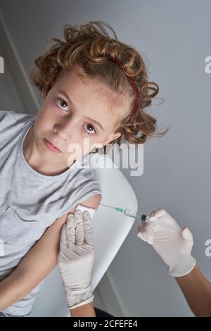 Unkenntlich Crop Arzt in Latex-Handschuhe Füllung in Spritze mit Impfstoffmedikament aus der Flasche, die für die Injektion in der Schulter vorbereitet Junge mit lockigen Haaren Stockfoto