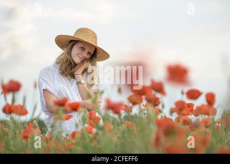 Junge Frau im Strohhut im Mohn Feld lächelt an Kamera Stockfoto