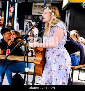 Junge Frau spielt Gitarre und singt, unterhaltsame Menschenmassen in Camden Market London UK Stockfoto