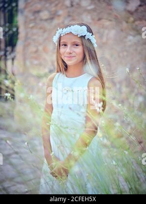 Portrait von kleinen niedlichen Mädchen tragen weiße schöne Kleid Blume Kopfbügel und Blick auf die Kamera Stockfoto