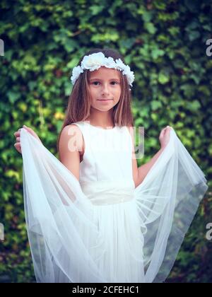 Portrait von kleinen niedlichen Mädchen tragen weiße schöne Kleid Blume Kopfbügel und Blick auf die Kamera Stockfoto