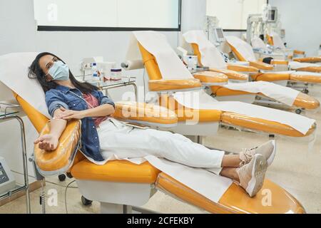 Weibliche Spenderin mit Pflaster auf der Hand sitzend im medizinischen Stuhl Nach Bluttransfusion Verfahren Stockfoto