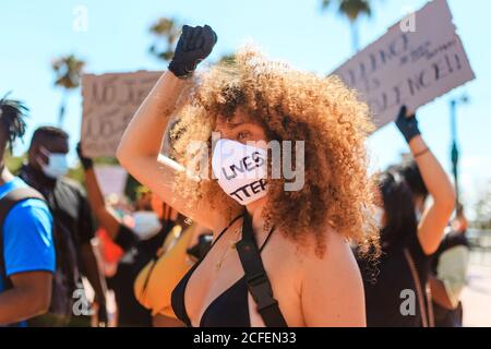 Ethnic weiblich mit afro Frisur und in Schutzmaske mit Black Lives Matter Inschrift steht auf der Straße und hebt die Faust während Eine Demonstration Stockfoto