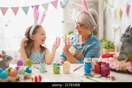 Frohe ostern! Eine Großmutter und ihre Enkelin malen Ostereier. Glückliche Familie bereitet sich auf Ostern vor. Nettes kleines Kind Mädchen trägt Hase Ohren o Stockfoto