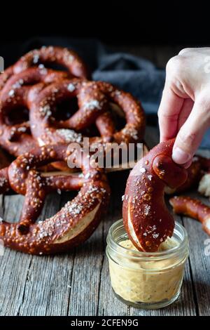 Crop Person Tauchen hausgemachte frische Brezel mit Salz in Käse Sauce auf Holztisch Stockfoto