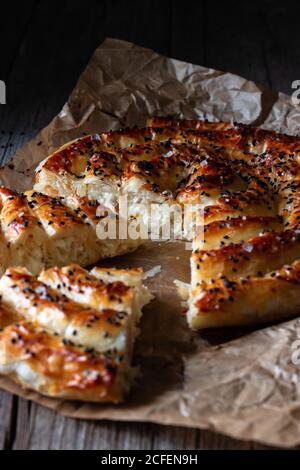 Crop Cook hält heiße Backform mit frischem Blätterteig Und Servierstück borek auf Teller Stockfoto