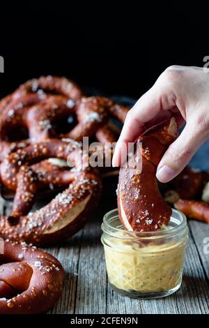 Crop Person Tauchen hausgemachte frische Brezel mit Salz in Käse Sauce auf Holztisch Stockfoto