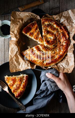 Von oben Ernte kochen hält heißen Auflaufform mit frisch Blätterteig und Servierstück borek auf Teller Stockfoto