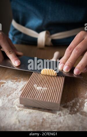 Anonyme weibliche Vorbereitung Teig für hausgemachte Gnocchetti Pasta auf einem Holzwerkzeug im Tisch in der Küche Stockfoto