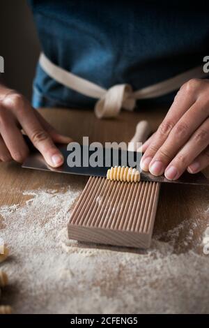 Anonyme weibliche Vorbereitung Teig für hausgemachte Gnocchetti Pasta auf einem Holzwerkzeug im Tisch in der Küche Stockfoto