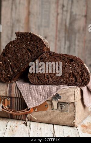 Appetitlich gesunder dunkler Roggenbrotkuchen mit eingeschnitten Körnern Halb auf Retro-Stoffkoffer auf schäbigen Holztisch gelegt Stockfoto