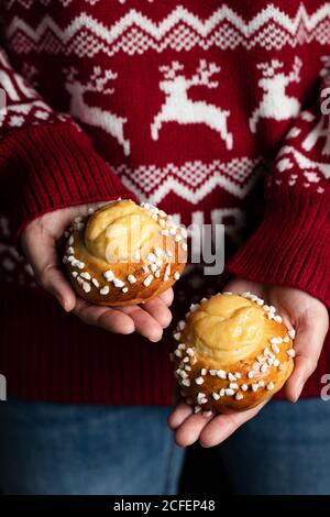 Crop weiblich in roten weihnachts-Pullover und Jeans mit hausgemachten Gebäck und Demonstration leckere frische Brötchen mit weißen Streuseln Stockfoto