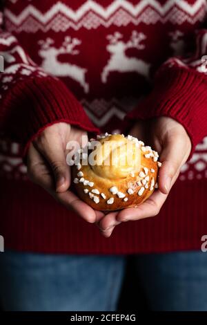 Crop weiblich in roten weihnachts-Pullover und Jeans mit hausgemachten Gebäck und Demonstration leckere frische Brötchen mit weißen Streuseln Stockfoto