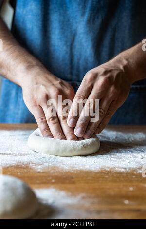 Unkenntlich Männchen in Schürze Abflachung weichen Teig über Tisch mit Mehl beim Kochen Pizza Stockfoto