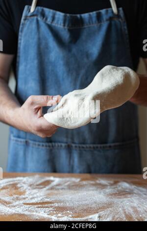 Unkenntlich Männchen in Schürze Abflachung weichen Teig über Tisch mit Mehl beim Kochen Pizza Stockfoto