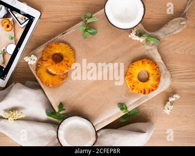 Blätter der frischen Minze auf Holzbrett in der Nähe von Scheiben gelegt Von süßer Ananas und Hälften von schmackhafter Kokosnuss auf Holz Tischplatte in der Nähe von Tablett und Serviette Stockfoto